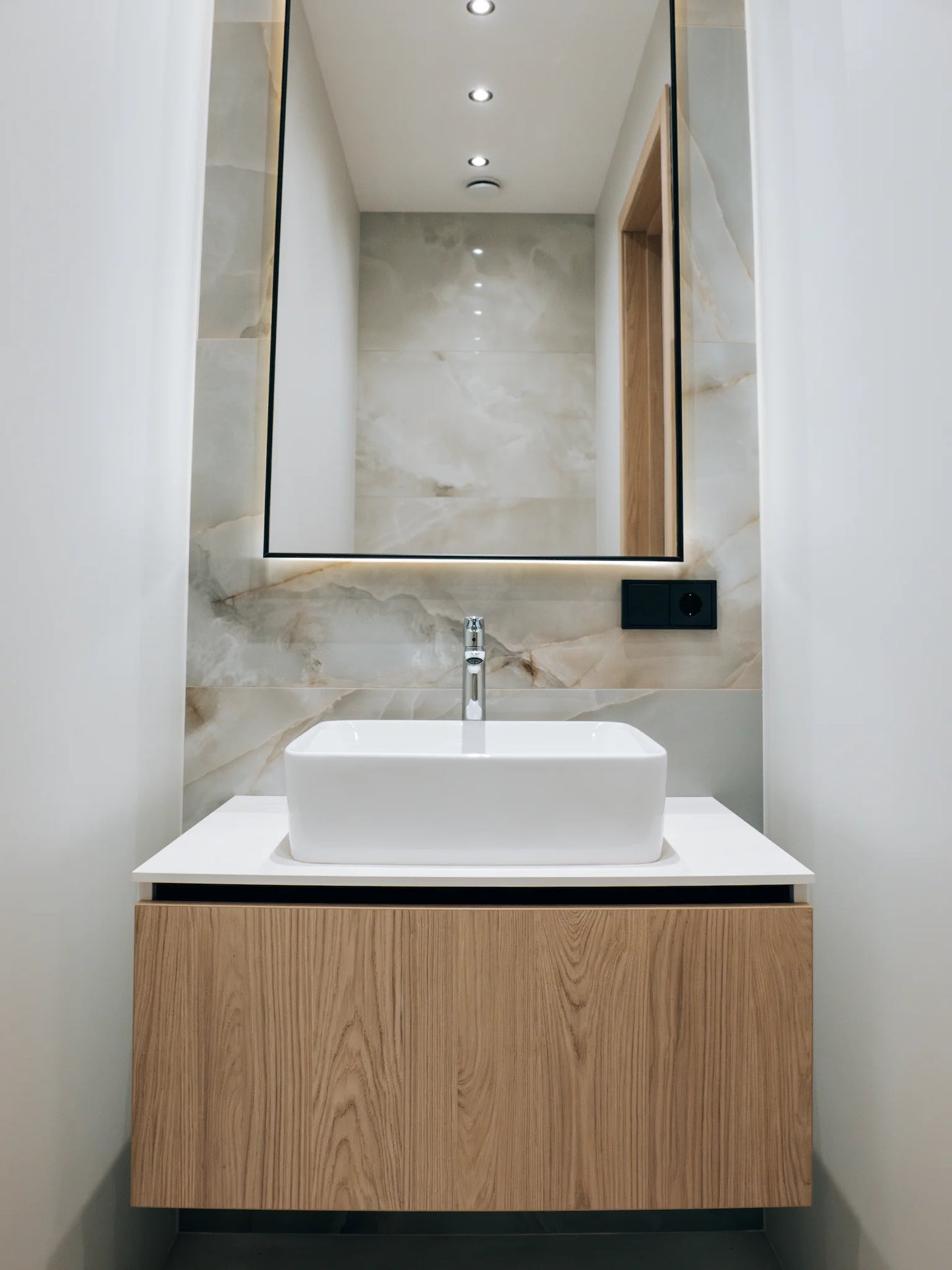 Modern bathroom with wooden vanity, white sink, and large mirror.