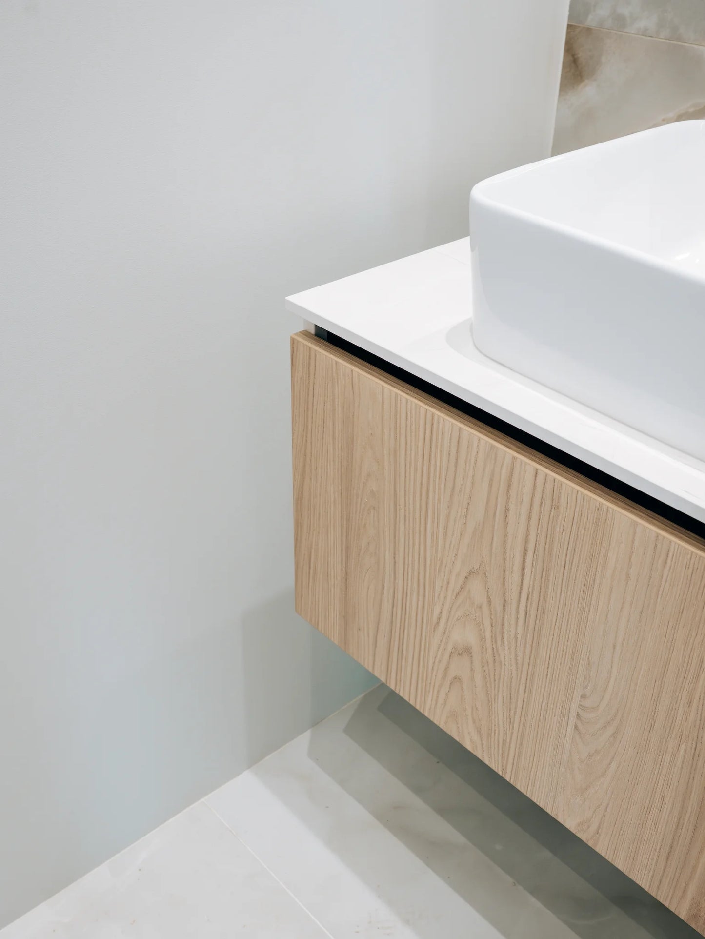 Bathroom vanity with wooden cabinet and white countertop against a light gray wall.