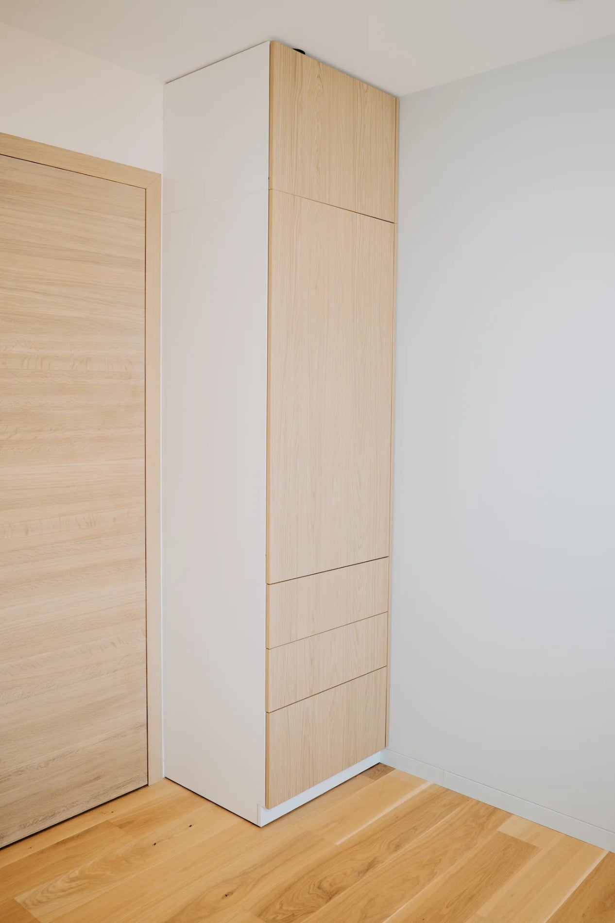 Tall white cabinet with wooden doors in a minimalistic room.
