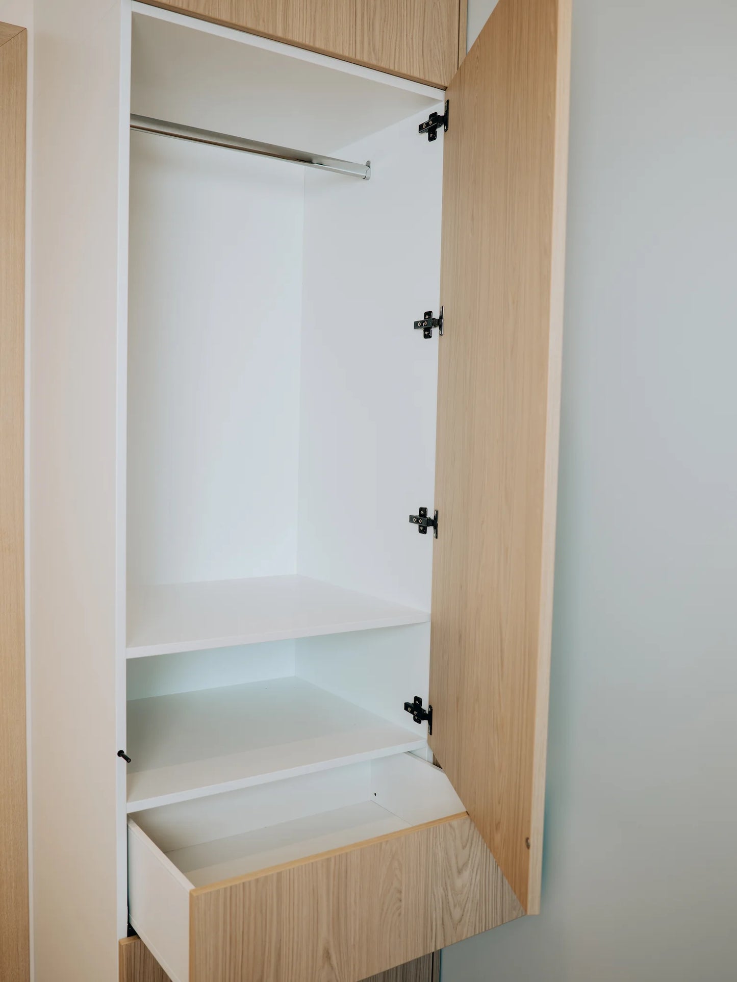 Open wooden wardrobe with shelves and a hanging rod inside.