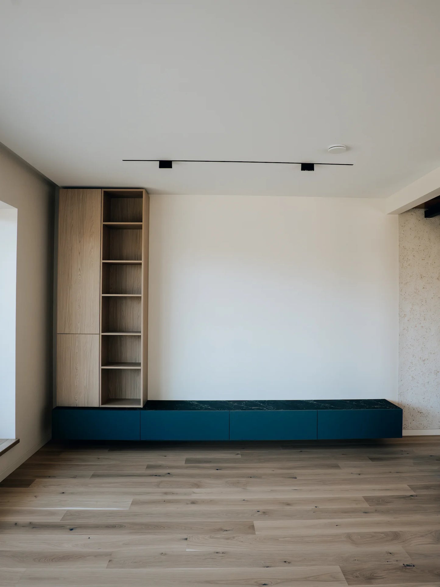 Modern interior with wooden bookshelf and blue entertainment console against a white wall.