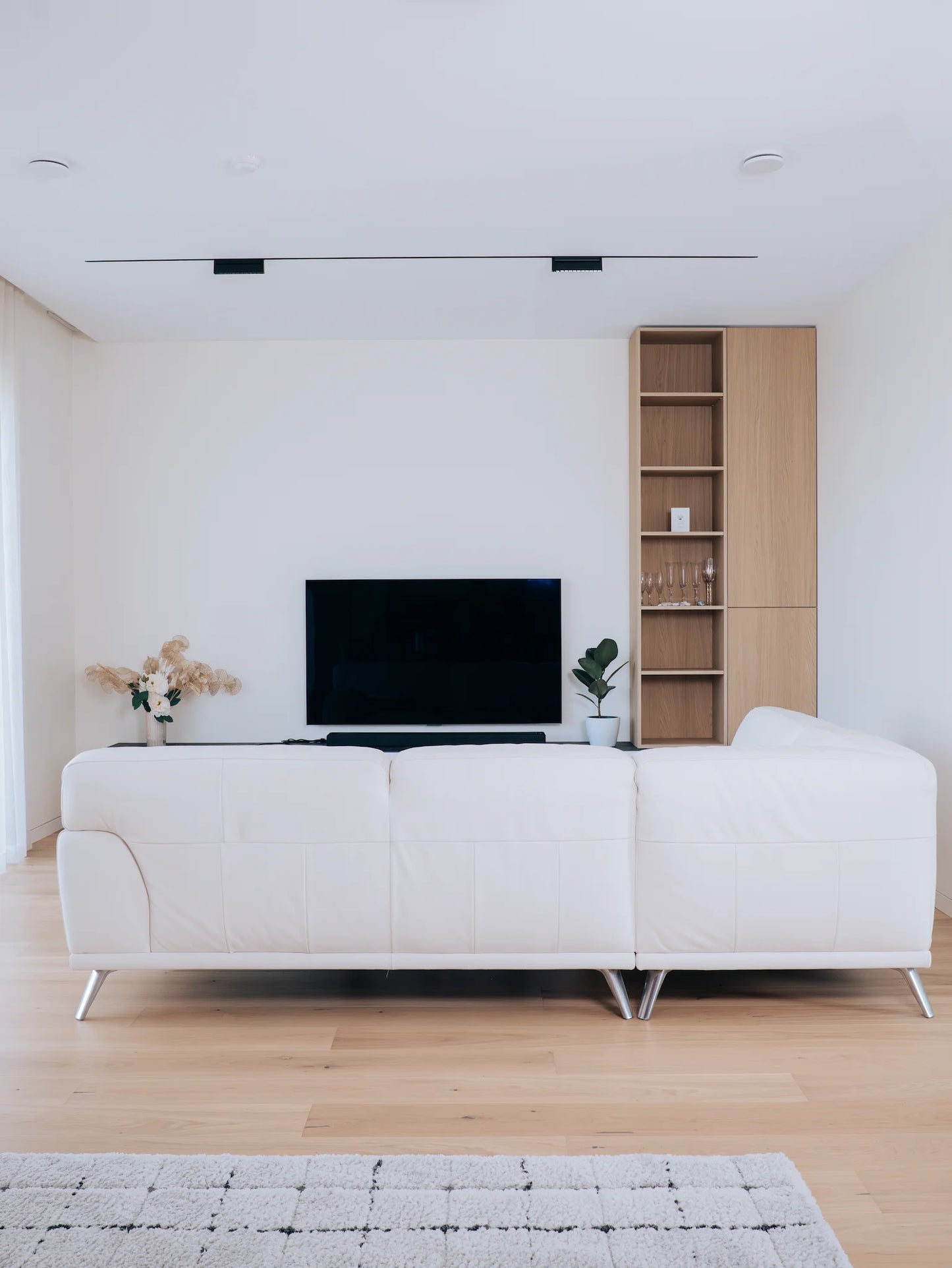Modern living room with a large flat-screen TV mounted on a white wall above a wooden shelf.