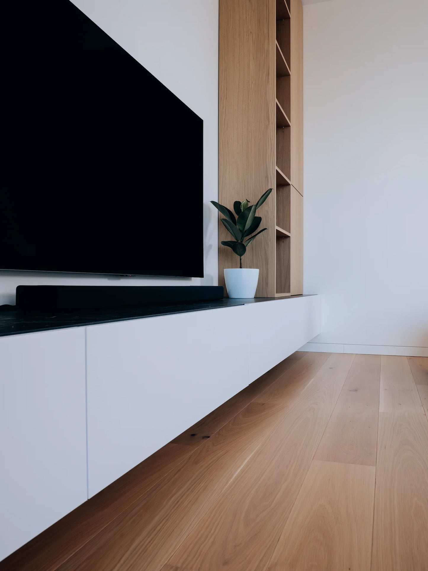 Modern living room with a large flat-screen TV mounted on a white wall above a wooden shelf.
