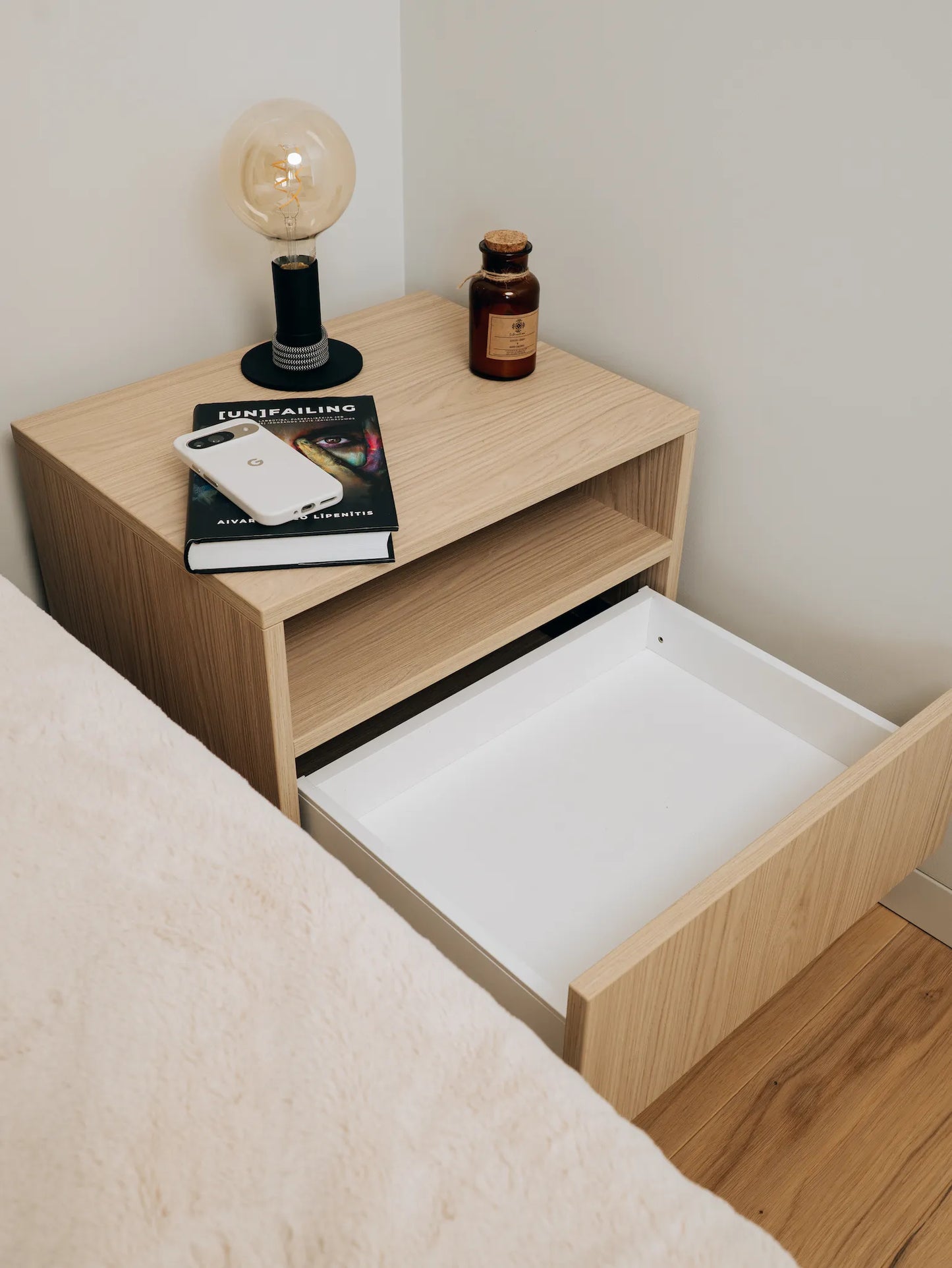 Wooden nightstand with open drawer, books, phone, and lamp on top.