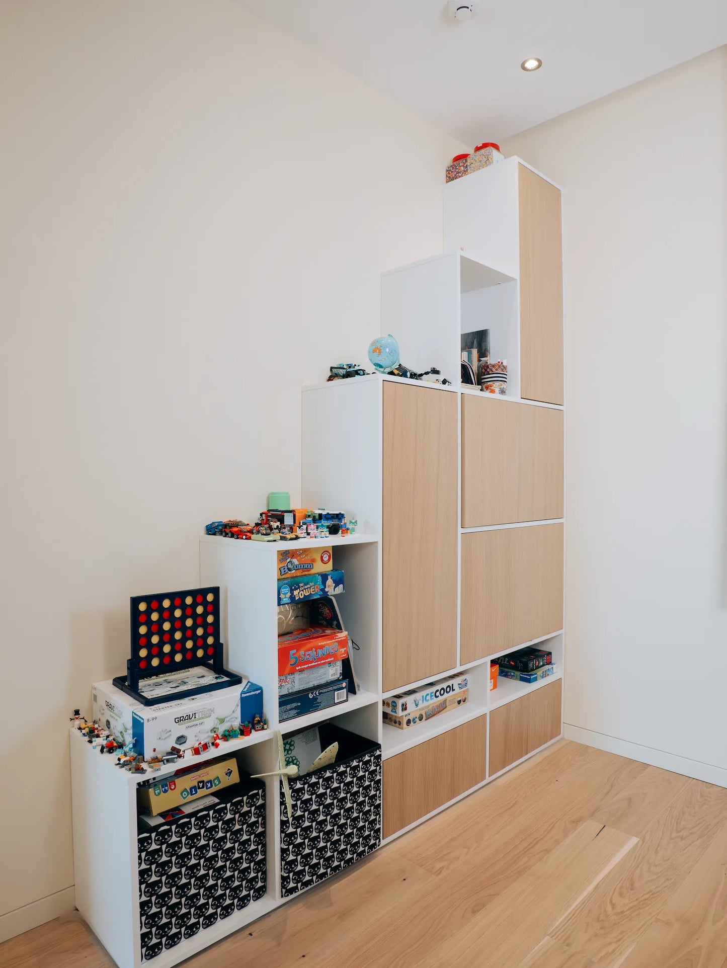 Children's toy storage unit with books and toys on a wooden floor.