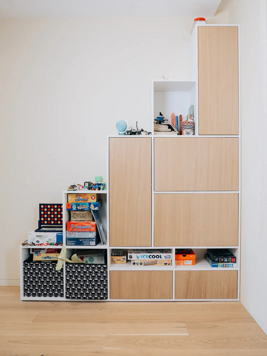 Modular wooden storage unit with books and toys on a wooden floor.