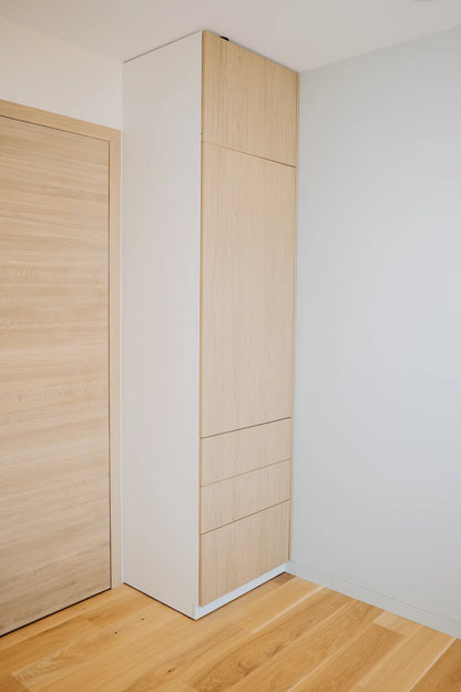 Tall white cabinet with wooden doors in a minimalistic room.