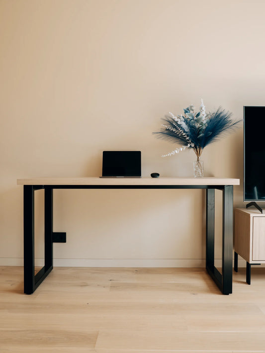 Modern desk with laptop, decorative vase, and TV in a minimalistic room.