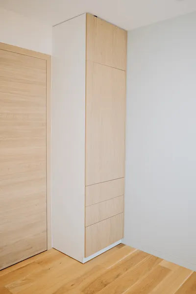 Tall white cabinet with light wood panels in a minimalistic room.