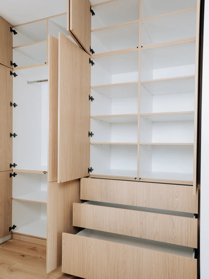Wooden wardrobe with open doors and drawers in a room.