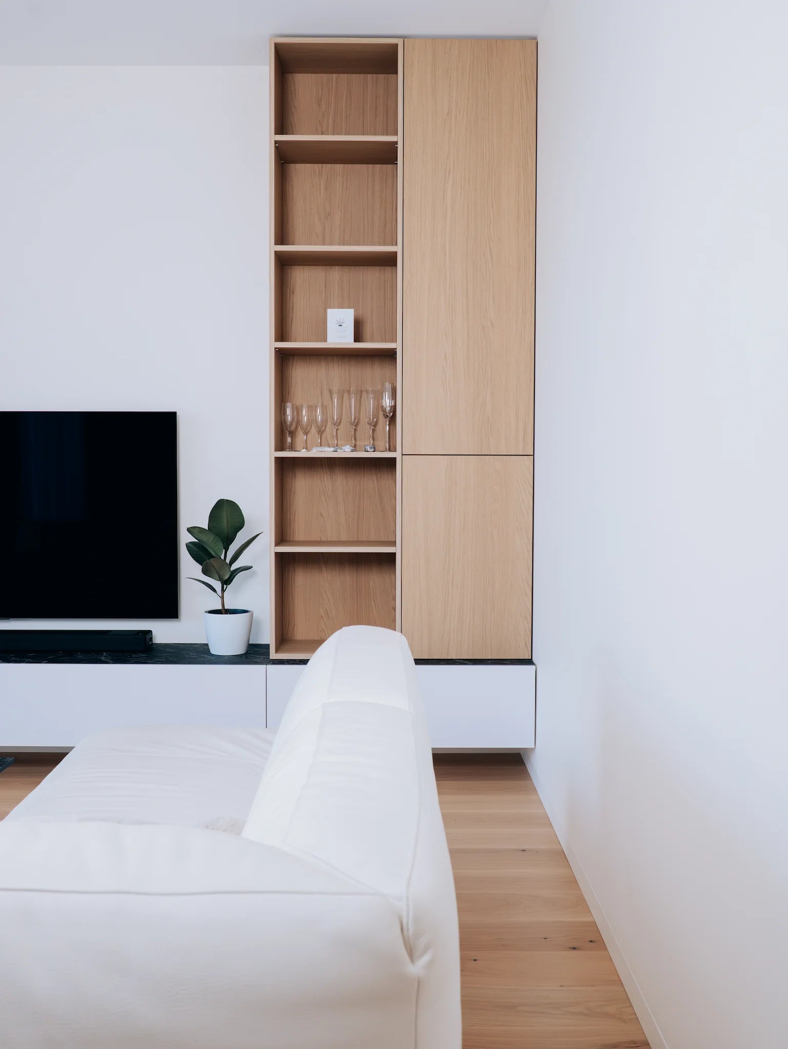Modern living room with a white sofa, wooden bookshelf, and TV.