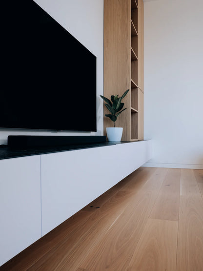 Modern living room with a large flat-screen TV mounted on a white wall above a wooden shelf.