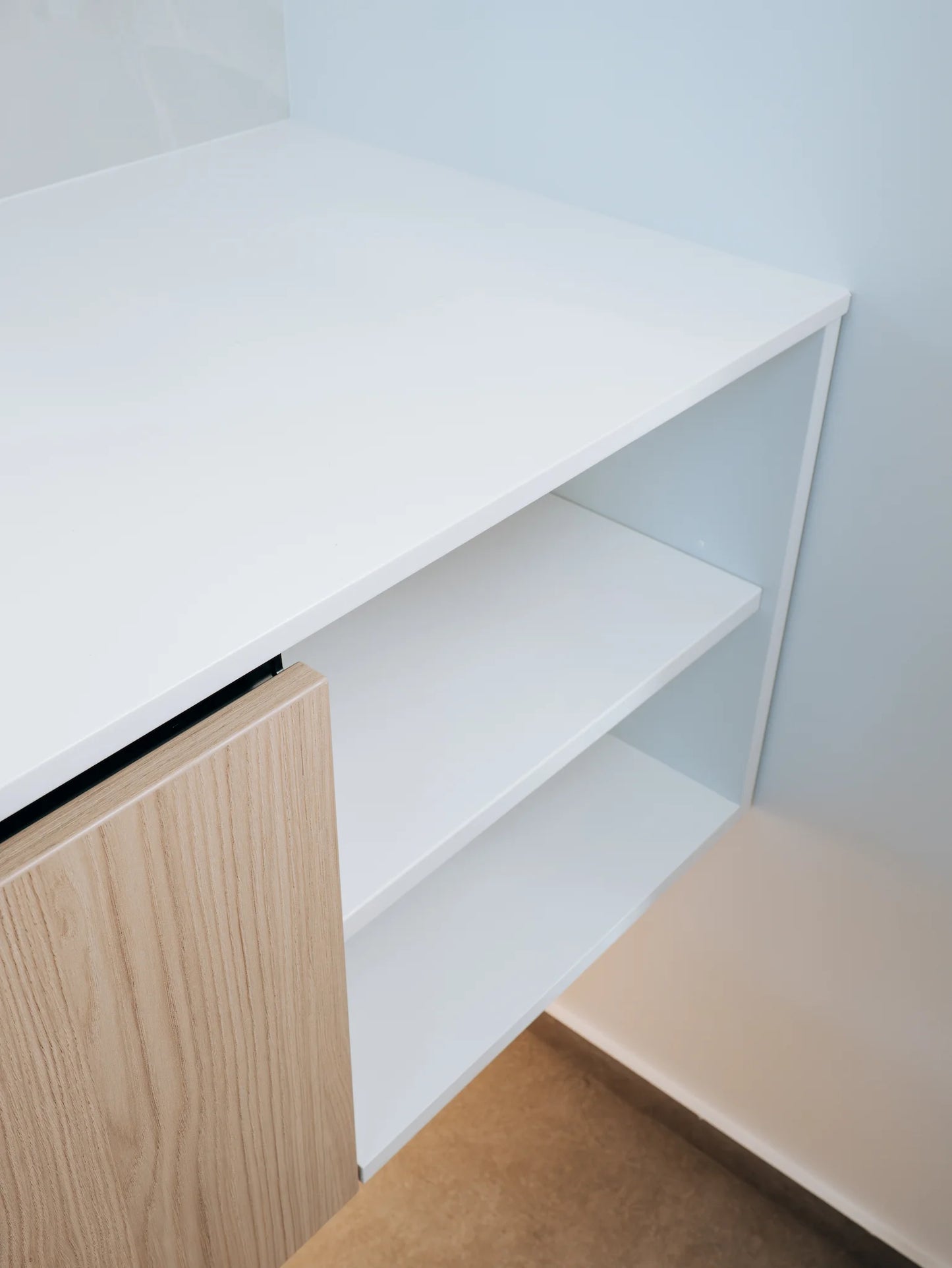 White desk with wooden side panel and chair in a minimalistic room.