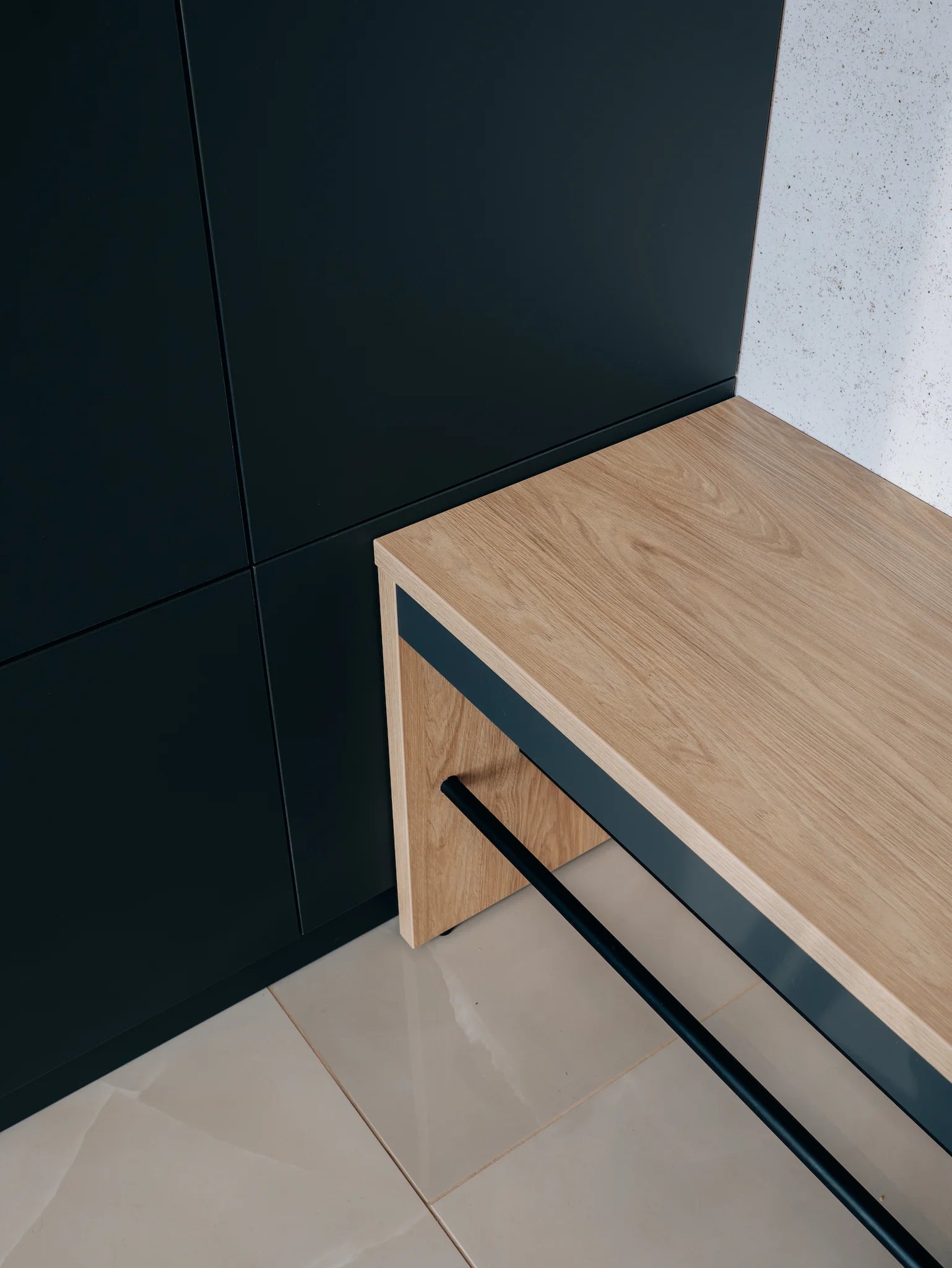 Wooden bench against a black wall with a light-colored floor.