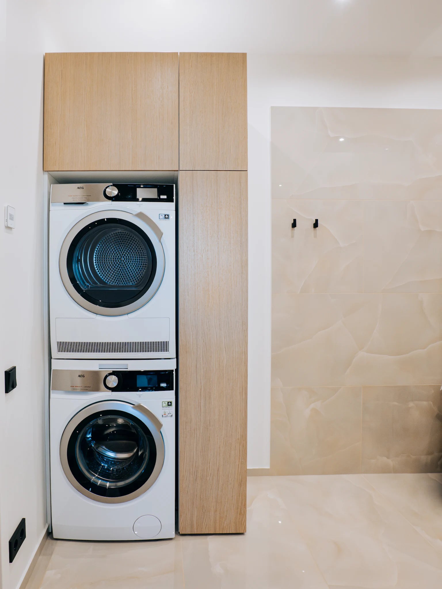 Stacked washer and dryer in a modern laundry room with wooden cabinets.