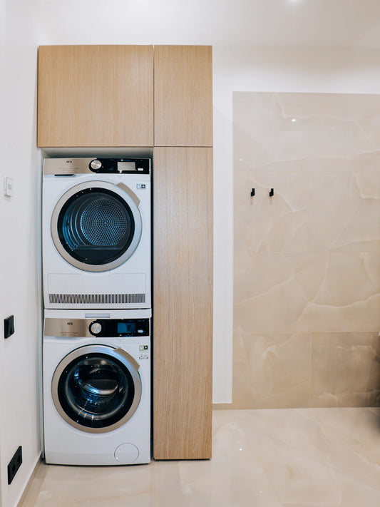 Stacked washer and dryer in a modern laundry room with wooden cabinets.
